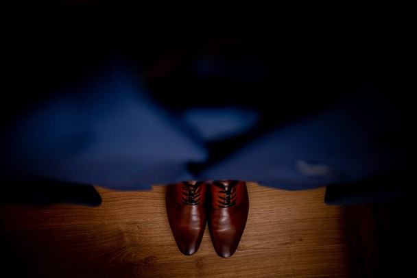 A top angle horizontal  shot of a male wearing brown shoes and a dark blue tuxedo standing on a brown hardwood floor - Photo, image
