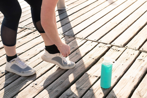 legs of an unrecognizable woman tying her running shoes next to her water bottle, concept of sport and healthy lifestyle, copy space for text - Foto, immagini