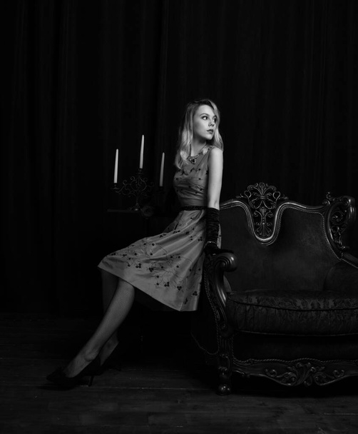 beautiful girl in a red dress posing in armchairs waiting on a black background - Fotó, kép