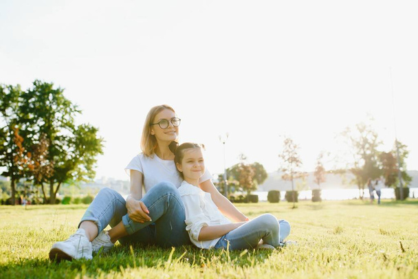 Happy and friendly family in nature. Emotional and young mother hugs her smiling little daughter lying on the grass. Summer park. Positive emotions.Childhood. Summertime.Lifestyle - Foto, imagen