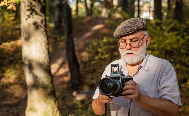Travel shoot. Photographer in forest. Lifestyle with autumn nature. retro photographic equipment. Mature man with beard. photographs green landscape. Photographer Taking Photo. Landscape Photography - Fotó, kép