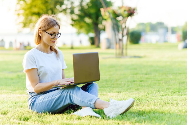 beautiful woman working with laptop in the park on the grass. The concept of remote work - Fotoğraf, Görsel