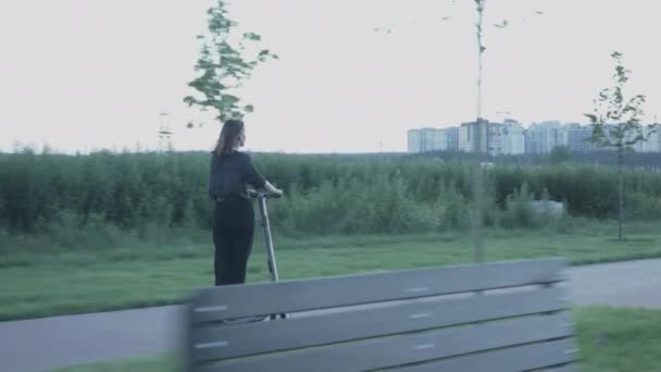 Girl moves on electric ecological scooter at city embankment at sunset. Young businesswoman in suit rides on e-scooter from office. Woman riding personal electric transport on promenade at sunset - Video