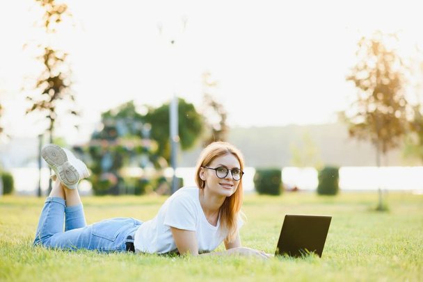 Portrait of a beautiful woman with a laptop lying on the grass - Фото, изображение