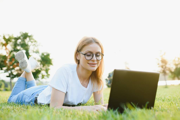 Beautiful and happy young woman lying on the grass surrounded by technology devices - Zdjęcie, obraz