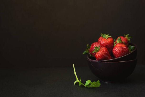 Fresh ripe strawberries with arugula in bowl on dark background. Copy space - Photo, Image