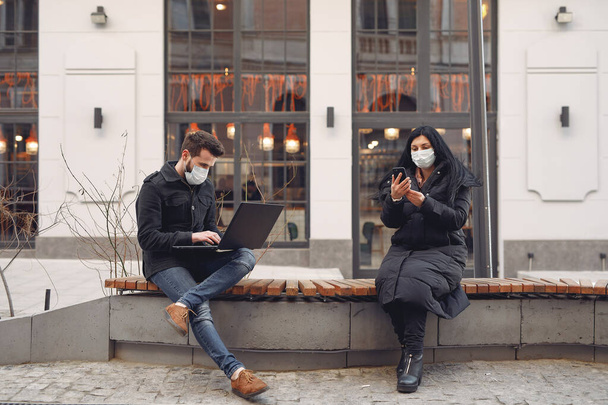 People in a masks sitting in a city with a laptop - 写真・画像