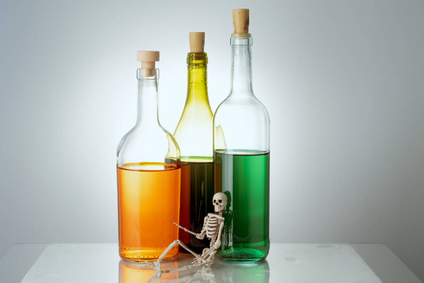 szkielet leży na tle trzech butelek z różnymi cieczami. koncepcja szkodliwości alkoholu - Zdjęcie, obraz