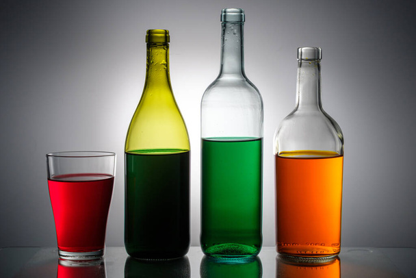рідини різних кольорів, розливаються в пляшки і скляні ємності встановлюються поспіль. скляні предмети на сірому фоні
 - Фото, зображення