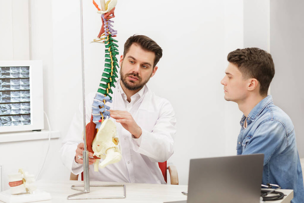 Doctor showing flexible spine model to his patient and explains the cause of his pain in medical office. Patient visiting physiotherapist in clinic. Surgery, healthcare and medicine concept - Fotoğraf, Görsel