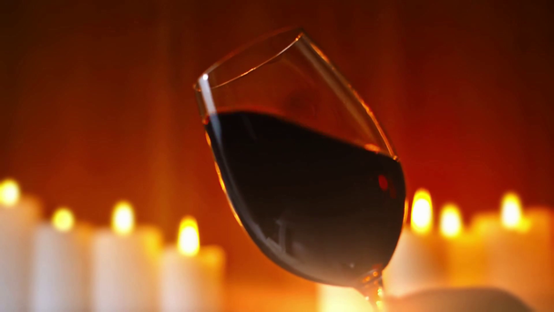 red splashing wine in wineglass with burning candles on background - Footage, Video