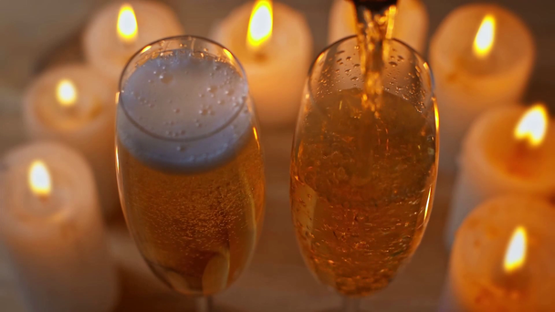 pezsgőspoharakba öntött pezsgőbor az égő gyertyák közelében - Felvétel, videó