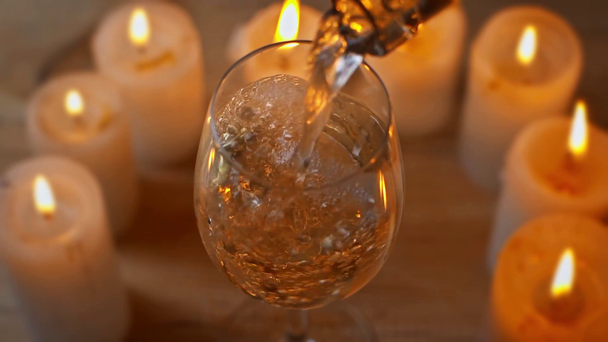 bílé víno nalévání v sklenici vína v blízkosti hořících svíček - Záběry, video