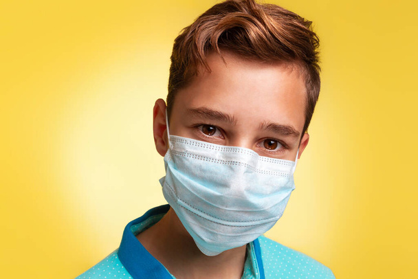 O conceito de proteção contra vírus e doenças. Retrato de perto de um adolescente com uma t-shirt azul e uma máscara. Fundo amarelo. Espaço de cópia
. - Foto, Imagem