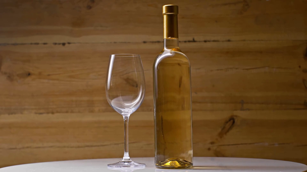 bottle of white wine near empty wineglass spinning on wooden background - Footage, Video