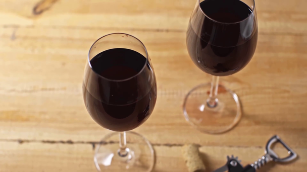 korek, korkociąg i kieliszki do wina z czerwonym winem na drewnianym tle - Materiał filmowy, wideo