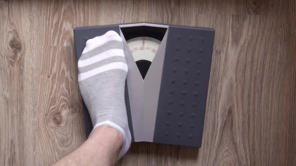 Man stapt op de mechanische vloerweegschaal om zijn gewicht te controleren. Het concept van het aanpakken van overgewicht en obesitas. - Video