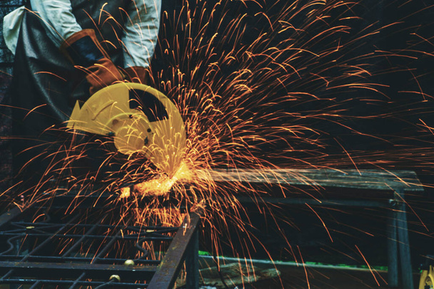 Руки человека с перчаткой с помощью электростальной режущей машины во время работы в цехе. Мужчина режет сталь искрами. Тяжелая работа на заводе или в гаражной промышленности в концепции строительных площадок. - Фото, изображение