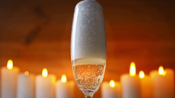 pezsgőspoharba öntött pezsgőbor az égő gyertyák közelében - Felvétel, videó