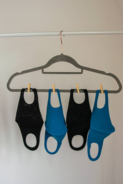 Foto van enkele herbruikbare gezichtsmaskers kleur blauw en zwart opknoping op een doek rek tijdens het drogen na het wassen. Witte achtergrond in een huis. Uitbraak van het coronavirus - Foto, afbeelding