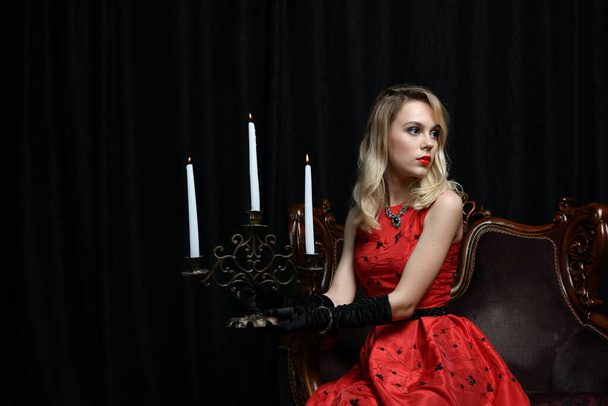 красива дівчина в червоній сукні позує в кріслі з червоною трояндою на чорному тлі
 - Фото, зображення