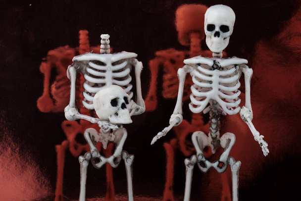 Dwa ludzkie szkielety stoją na powierzchni lustra, jeden z nich trzyma głowę w rękach. Koncepcja jest jasna nie trać głowy - Zdjęcie, obraz