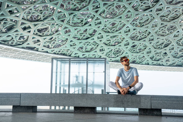 Abu Dhabi, United Arab Emirates, MAY 20, 2020: Young man sitting in louvre in Abu Dhabi exploring the art. - Φωτογραφία, εικόνα