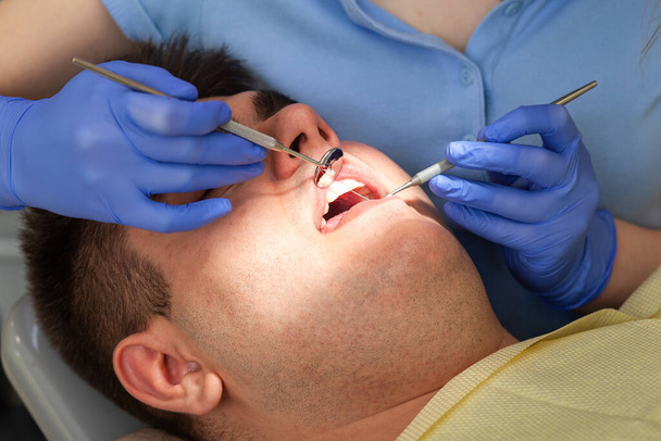 Επισκέπτεται γυναίκα οδοντίατρο στην κλινική. Νεαρός άνδρας που κάθεται ορθάνοιχτος στο γραφείο του οδοντιάτρου στην ετήσια εξέταση. Γιατρό κορίτσι - Φωτογραφία, εικόνα