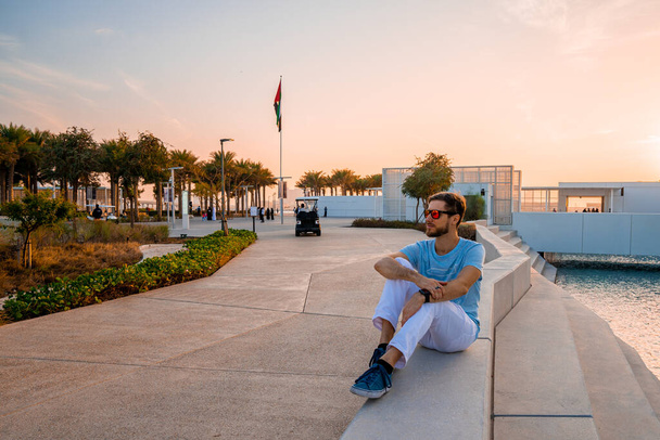 Louvre, Abu Dhabi, United Arab Emirates - May 10, 2020.  Young man sitting by the louvre in Abu Dhabi. Beautiful building at sunset. - 写真・画像