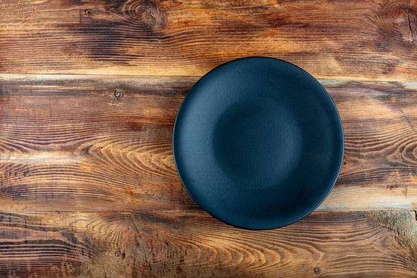 Black empty serving plate on the wooden table. Black round plate on wooden background, top view, copy space. - Foto, afbeelding