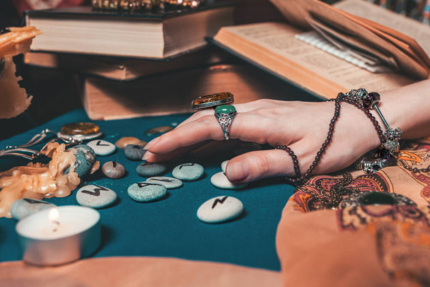 Astrologia ed esoterismo. La mano femminile della strega legge le rune. Sullo sfondo, vecchi libri, rune lungimiranti, candele e gioielli. Da vicino.. - Foto, immagini
