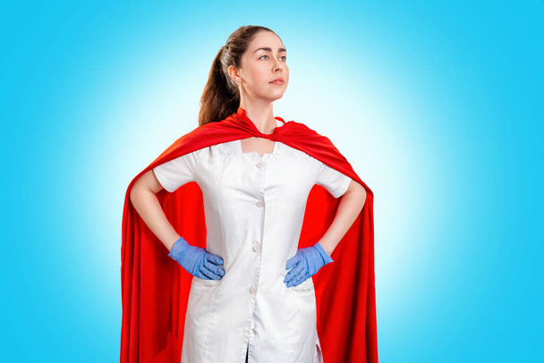 Um médico usando luvas médicas, e uma capa vermelha de super-herói fica de guarda sobre a saúde. Fundo azul. Espaço para cópia. O conceito do Poder de um super-herói para a medicina
. - Foto, Imagem