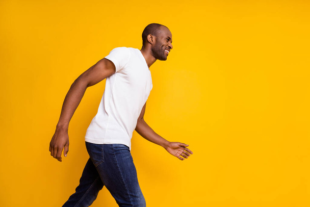 Profile photo of attractive dark skin guy man walking moving down street cheerful good mood wear casual white t-shirt jeans isolated yellow vibrant color background - Фото, зображення