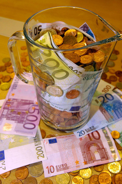 κέρματα ευρώ και χαρτονομίσματα σε γυάλινη κανάτα πάνω σε τραπέζι - Φωτογραφία, εικόνα