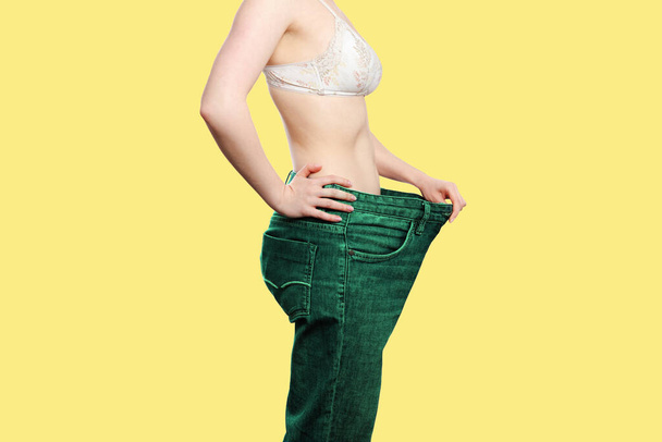 Белая женщина показывает результаты своей потери веса, дергая широкоталевые зеленые джинсы. Изолировать, желтый фон. Вид сбоку. Принято. Концепция потери веса, спорта и диеты
. - Фото, изображение