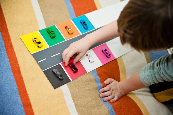 Makineleri renklerine göre ayıran bir çocuk. Montessori konsepti, erken eğitim. Evde yapılması kolay fikirler. Renkli kağıt üzerinde daha nazik sürpriz arabalar.. - Fotoğraf, Görsel