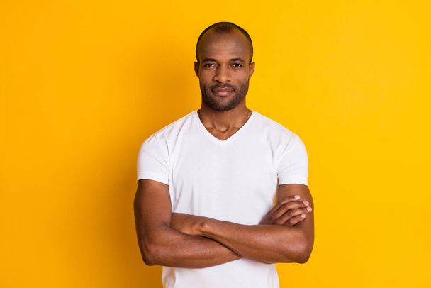 Photo of cheerful dark skin guy good mood hold arms crossed self-confident business man wear casual white t-shirt isolated bright vivid yellow color background - Fotoğraf, Görsel