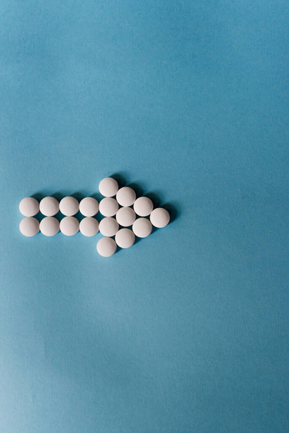 Stock photo of a bunch of different pills placed on a blue background in the shape of an arrow. There is nobody on the picture. - Foto, Bild