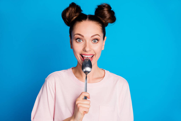 Photo of pretty lovely satisfied lady two funny buns metal spoon inside mouth lick try tasty meal overjoyed tricky wear casual pink t-shirt isolated bright blue color background - Foto, afbeelding