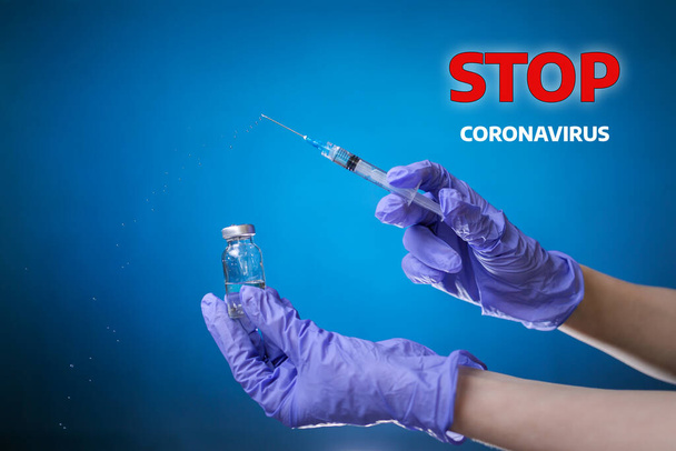 コロナウイルスを止めて。医療用手袋の医師の手は注射用のバイアルと注射器を保持しています。青の背景。コロナウイルス、ワクチン、健康の概念。スペースのコピー. - 写真・画像