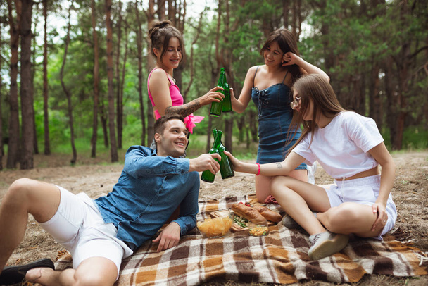 Group of friends clinking beer bottles during picnic in summer forest. Lifestyle, friendship - Фото, зображення