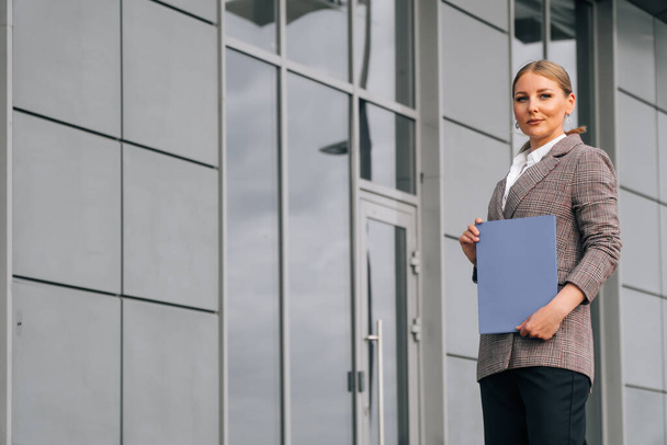 Stylish elegant woman of European appearance holds a folder with documents. The concept of a business lady against the background of the business center - Φωτογραφία, εικόνα