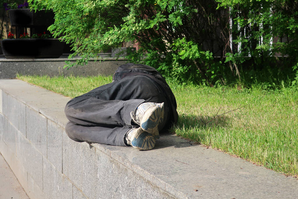 ένας άντρας με αθλητικά παπούτσια ξαπλωμένος σε ένα γρανιτένιο πεζοδρόμιο δίπλα στο γκαζόν - Φωτογραφία, εικόνα