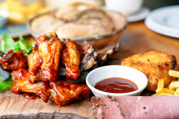 Vegyes húsok, grillezett bordák, sültkrumplis csirkeszárnyak szelektív fókusza fából készült tányéron, Top view Mixed bbq meat plate. - Fotó, kép