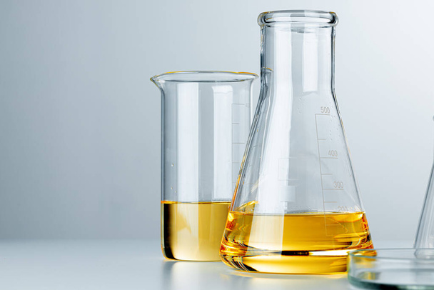 Laboratory glassware with yellow oily liquid on grey background - Foto, Imagem