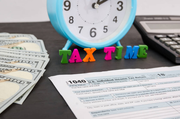 Belastingformulier 1040, wekker, rekenmachine, dollars en het woord "belastingtijd"". - Foto, afbeelding