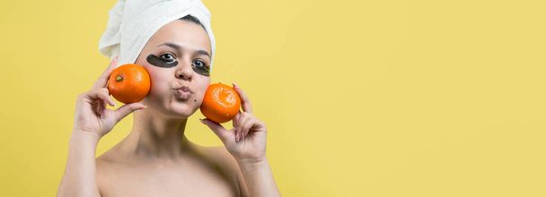 Beauty portrait of woman in white towel on head with gold nourishing mask on face. Skincare cleansing eco organic cosmetic spa relax concept. A girl stands with her back holding an orange mandarin. - Fotoğraf, Görsel