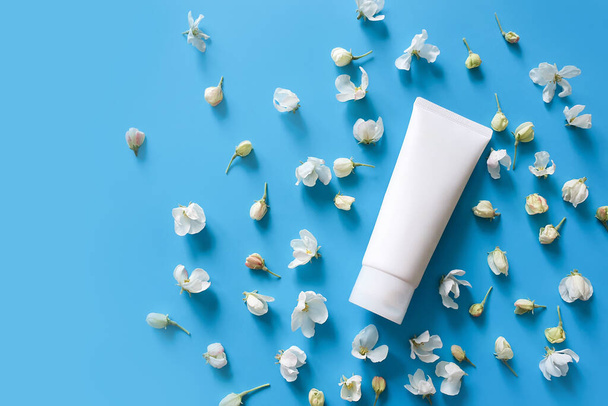 Top view of mock up of white squeeze bottle plastic tube for branding of medicine or cosmetics - cream, gel, skin care, toothpaste. Duds of blooming sakura on a blue background. Spa cosmetic product - 写真・画像