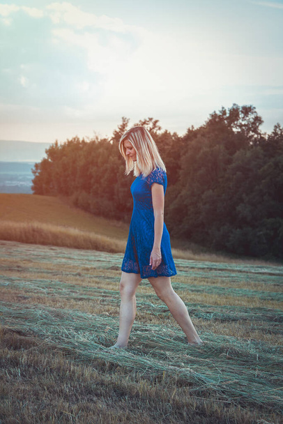 Ομορφιά ξανθά μαλλιά νεαρή γυναίκα με μπλε φόρεμα περπατώντας σε κουρεμένο γρασίδι. Διακριτά χρώματα - Φωτογραφία, εικόνα