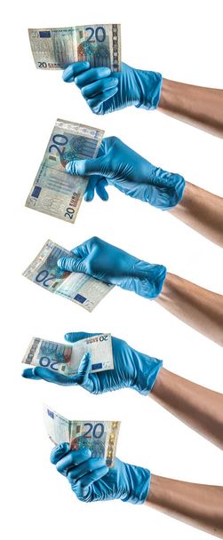 Some hands with blue latex glove holding a twenty euros bill - 写真・画像